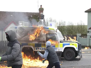 Pemuda bertopeng melemparkan bom molotov ke mobil polisi saat pengunjuk rasa Republikan yang menentang Perjanjian Jumat Agung mengadakan pawai di Londonderry, Irlandia Utara, Senin (10/4/2023). (AP Photo/Peter Morrison)
