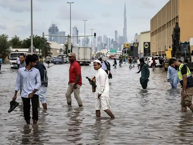 Orang-orang menerobos genangan air banjir setelah hujan lebat di Dubai, Uni Emirat Arab (UEA) pada Jumat 19 Desember 2025. Hujan lebat yang terjadi pada Jumat 19 Desember 2025 berimbas pada genangan banjir di sejumlah ruas jalan di Dubai, Uni Emirat Arab (UEA). (FADEL SENNA/AFP)