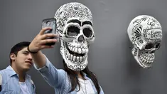 Seorang wanita berswafoto dengan replika tengkorak saat pameran dan kontes di perayaan Hari Kematian di Mexico City (1/11). Pameran dan kontes ini diadakan oleh Historic Center Foundation dalam rangka perayaan Hari Orang Mati. (AFP Photo/Yuri Cortez)