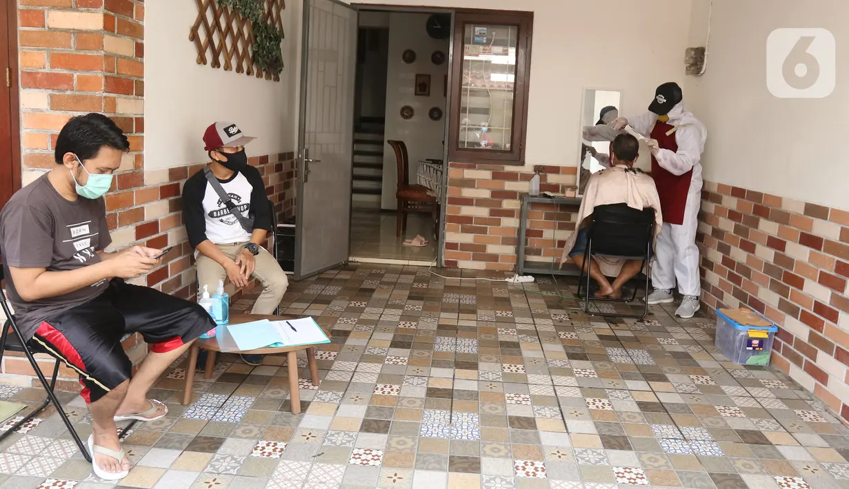 Tukang cukur mengenakan APD saat memotong rambut di halaman rumah pelanggan, Kelapa Dua, Depok, Jawa Barat, Senin (27/4/2020). Penerapan PSBB Kota Depok membuat tukang cukur tersebut menerima jasa panggilan ke rumah dan mengenakan APD untuk mencegah penularan COVID-19. (Liputan6.com/Herman Zakharia)