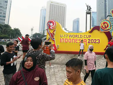 Masyarakat berswafoto dengan latar belakang papan promosi Piala Dunia U-17 2023 saat car free day (CFD) di kawasan Jalan Thamrin, Jakarta, Minggu (15/10/2023). Kegiatan tersebut dalam rangka promosi ajang Piala Dunia U-17 2023 di Indonesia. (Liputan6.com/Faizal Fanani)