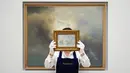 Seorang staf memegang lukisan 'Cloud Study' karya John Constable dengan latar belakang 'Study for Clouds' karya Gerhard Richter di Sotheby's, London, Inggris, 22 Juni 2022. Lukisan yang akan dilelang pada 29 Juni 2022 itu diperkirakan memiliki harga 100.000-150.000 pound, sedangkan 'Study for Clouds' 6-8 juta pound. (AP Photo/Alberto Pezzali)