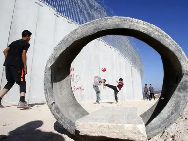 Anak-anak Palestina bermain sepak bola di sebuah lapangan di samping tembok pemisah Israel - Palestina di desa Beit Awa di Tepi Barat yang diduduki Israel (12/11). (AFP Photo/Hazem Bader)