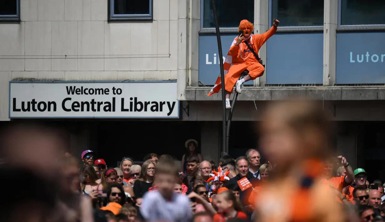 Seorang pendukung Luton Town menyambut kedatangan parade bus timnya melewati jalanan di Luton, Inggris setelah berhasil promosi ke Liga Inggris musim 2023/2024 pada Senin (29/05/2023) waktu setempat. The Hatters sukses menyegel tiket promosi setelah memenangkan laga play-off divisi Championship melawan Covetry City 6-5 melalui adu penalti di Wembley, Sabtu (27/5/2023). (AFP/Daniel Leal)