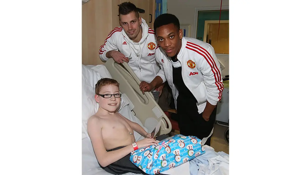 Seorang anak yang sedang sakit tampak senang menerima kado natal dari pemain Manchester United, Anthony Martial dan Morgan Schneiderlin. (www.manutd.com)