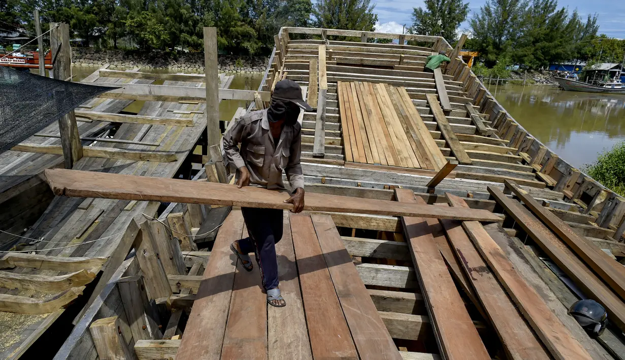 Pekerja memuat material untuk membuat kapal nelayan di Banda Aceh, Aceh pada 21 November 2020. Industri galangan kapal tradisional di daerah itu mengalami kesulitan memperoleh bahan baku kayu untuk memproduksi kapal nelayan, sehingga berdampak pada proses penyelesaian kapal. (CHAIDEER MAHYUDDIN/AFP)