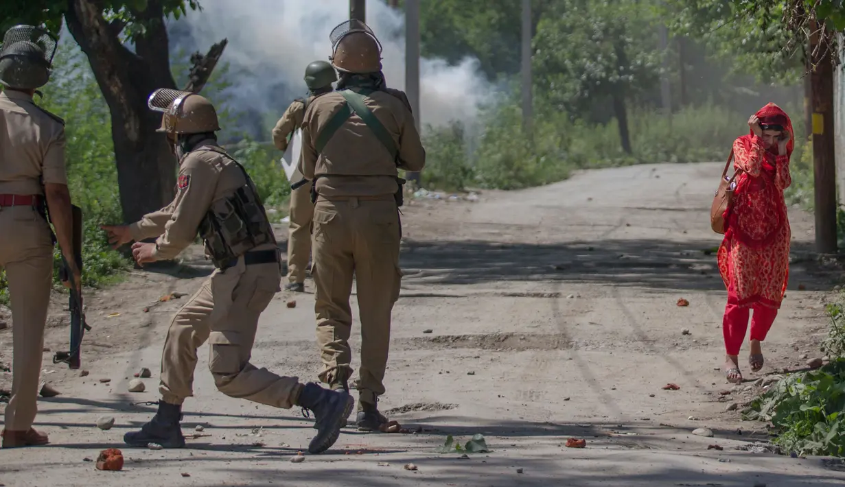 Seorang wanita berjalan disamping polisi India saat bentrokan di Srinagar, Kashmir yang dikuasai India, (23/5). Bentrokan telah meningkat setelah tentara menggerebek sebuah perguruan tinggi di kota selatan Pulwama bulan lalu. (AP Photo/Dar Yasin)