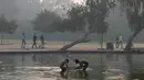 Anak-anak mandi di air kolam hias dekoratif yang menghiasi taman-taman yang mengelilingi monumen Gerbang India di tengah kondisi kabut asap tebal di New Delhi (30/10). (AFP Photo/Dominique Faget)