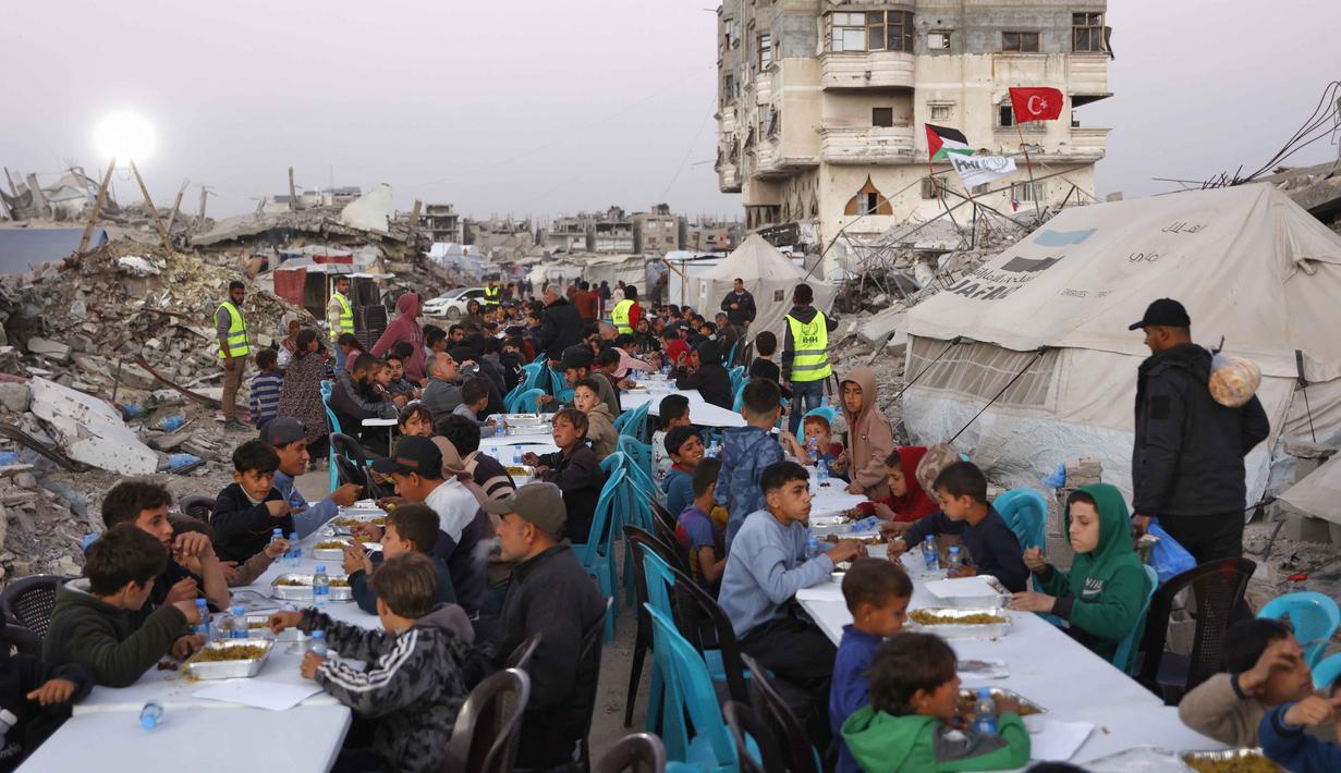 Sebagai informasi, ini merupakan Ramadan pertama sejak kesepakatan gencatan senjata antara Israel dan Hamas yang dimediasi Amerika Serikat pada 10 Oktober 2025. Tampak dalam foto, warga Palestina berkumpul untuk berbuka puasa bersama yang diselenggarakan oleh Yayasan IHH Turki, di tengah reruntuhan bangunan yang hancur di Kota Gaza pada Rabu 18 Februari 2026. (Omar AL-QATTAA/AFP)