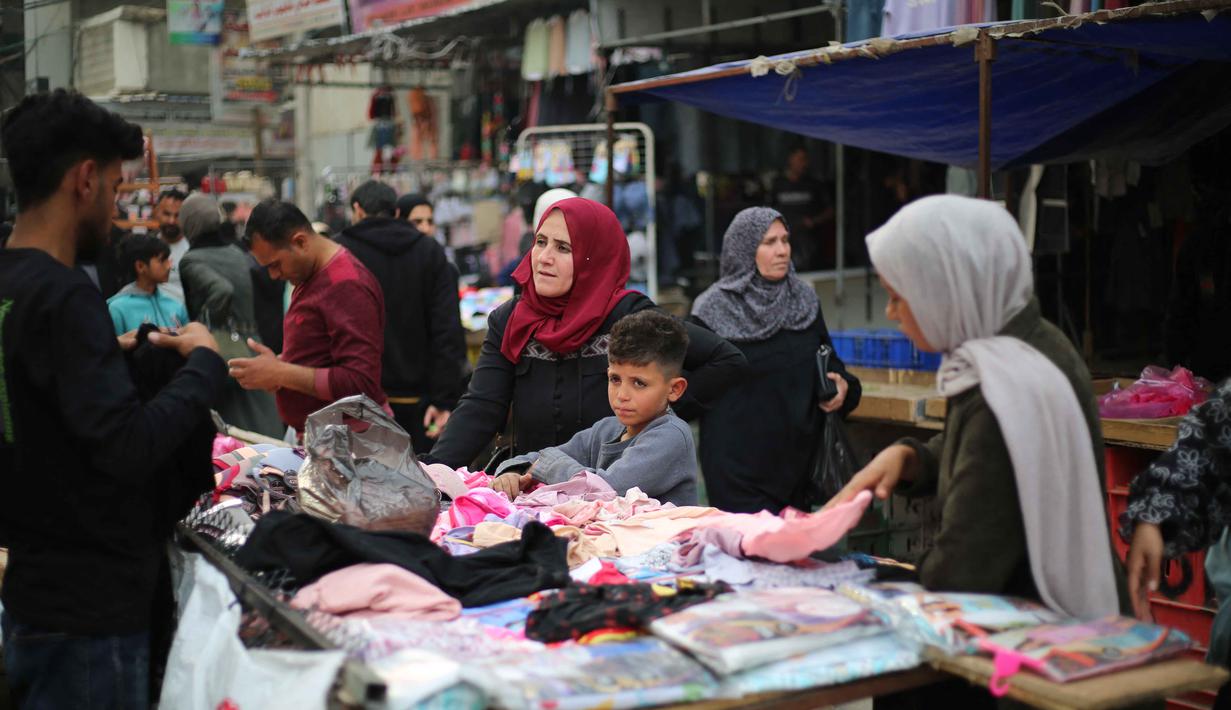 Sebagaimana diketahui, Badan Bantuan dan Pekerjaan PBB untuk pengungsi palestina, UNRWA telah mengumumkan 1,9 juta orang telah mengungsi secara paksa di Jalur Gaza Palestina. Tampak dalam foto, warga Palestina yang mengungsi berbelanja pakaian di pasar jalanan sekitar kamp pengungsi Nuseirat, Jalur Gaza tengah, pada Rabu 18 Maret 2026. (Eyad Baba/AFP)
