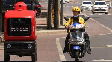 Seorang petugas pengiriman melewati kendaraan pengiriman otonom dari JD.com di jalanan Beijing, China, Jumat (28/5/2021). Raksasa e-commerce China JD.com meningkatkan operasi kendaraan pengiriman tak berawak. (AP Photo/Ng Han Guan)