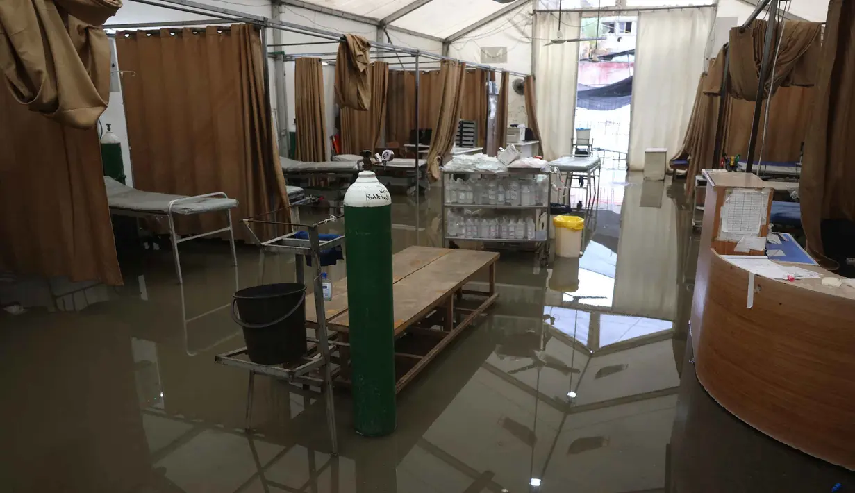 Hal ini untuk menghindari risiko infeksi bagi pasien. Tampak dalam foto, genangan air menutupi lantai tenda darurat milik Rumah Sakit Nasser, yang berfungsi sebagai tempat penerimaan pasien rawat jalan dan departemen gawat darurat, setelah hujan lebat di Khan Yunis di Jalur Gaza selatan pada 26 Maret 2026. (Bashar Taleb/AFP)
