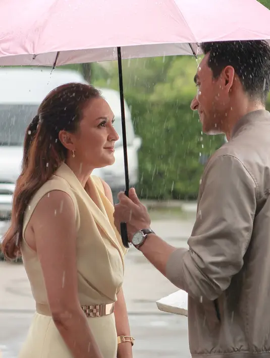 Darius tampak gagah memayungi Donna yang mengenakan gaun krem elegan. Mereka saling menatap penuh cinta seolah tak peduli dengan rintik hujan yang membasahi sekitar. Senyum Donna yang lembut semakin memperkuat kesan hangat di antara mereka. Liputan6.com/IG/@darius_sinathrya)