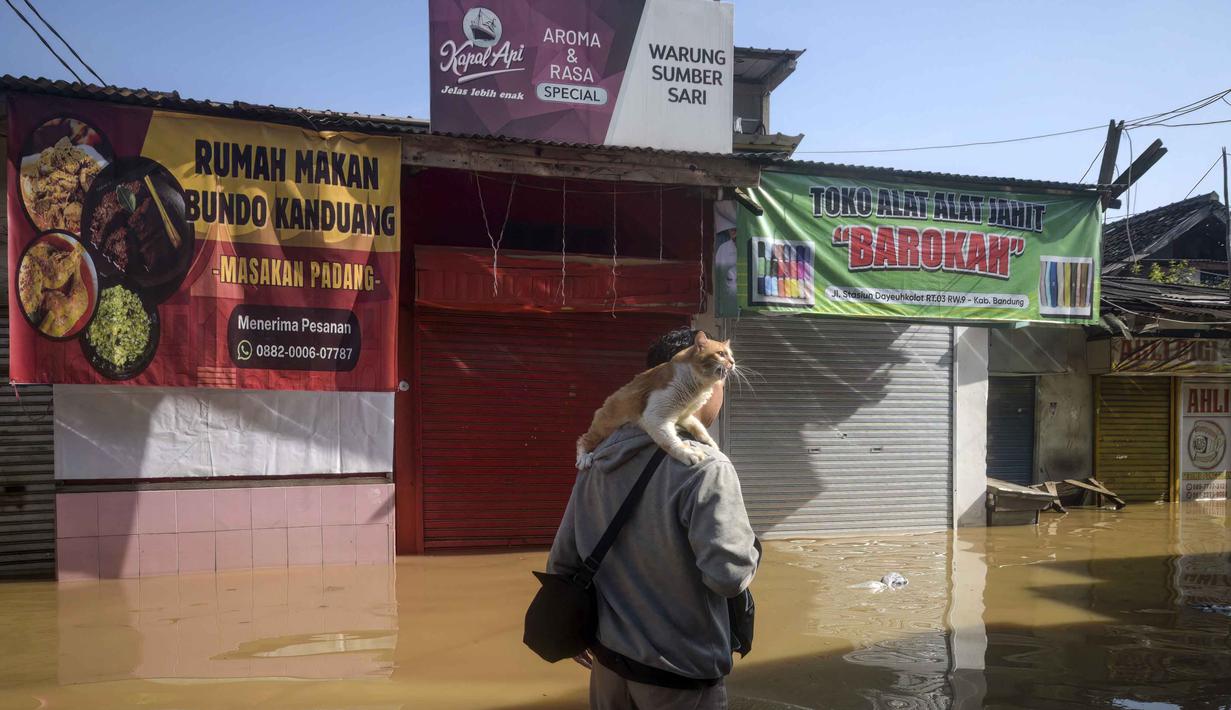 Badan Penanggulangan Bencana Daerah (BPBD) Kabupaten Bandung mencatat tiga kecamatan terendam banjir akibat luapan Sungai Citarum. Tampak dalam foto, seorang pria mengevakuasi kucingnya sambil mengarungi jalan yang terendam banjir di Bandung, Jawa Barat, pada Jumat 5 Desember 2025. (TIMUR MATAHARI/AFP)