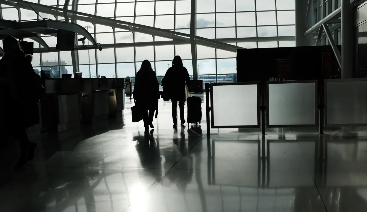 Orang-orang berjalan melalui terminal keberangkatan internasional yang sepi di Bandara John F. Kennedy (JFK), New York City, Sabtu (8/3/2020). Maskapai penerbangan terpukul wabah virus corona (COVID-19) setelah pelancong bisnis maupun rekreasi membatalkan rencana. (Spencer Platt/Getty Images/AFP)