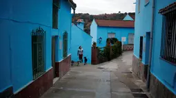 Seorang wanita bersama anjingnya berjalan di antara bangunan serba biru di Juzcar, Selatan Spanyol, 2 Desember 2016. Penduduk setempat menghabiskan 4.000 liter cat biru untuk merubah Juzcar menjadi sebuah tempat bernuansa Smurf. (REUTERS/Jon Nazca)