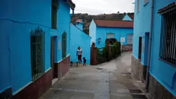 Seorang wanita bersama anjingnya berjalan di antara bangunan serba biru di Juzcar, Selatan Spanyol, 2 Desember 2016. Penduduk setempat menghabiskan 4.000 liter cat biru untuk merubah Juzcar menjadi sebuah tempat bernuansa Smurf. (REUTERS/Jon Nazca)