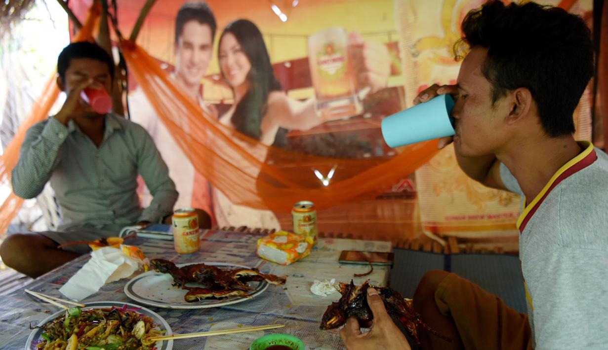Dua pria minum bir ketika menikmati tikus bakar di sebuah kios di provinsi Battambang, Kamboja (8/8/2019). Tikus bakar yang tusuk sate harganya masing-masing 0,25 USD atau sekitar 3500 rupiah. (AFP Photo/Tang Chhin Sotthy)