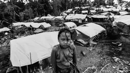 Seorang anak perempuan pose dengan latar belakang puluhan rumah Suku Baduy Luar setelah terbakar di Kampung Cisaban II, Desa Kanekes, Banten, Kamis (1/6). Kebakaran pada pekan lalu yang menghanguskan 83 rumah Suku Baduy Luar. (Liputan6.com/Fery Pradolo)