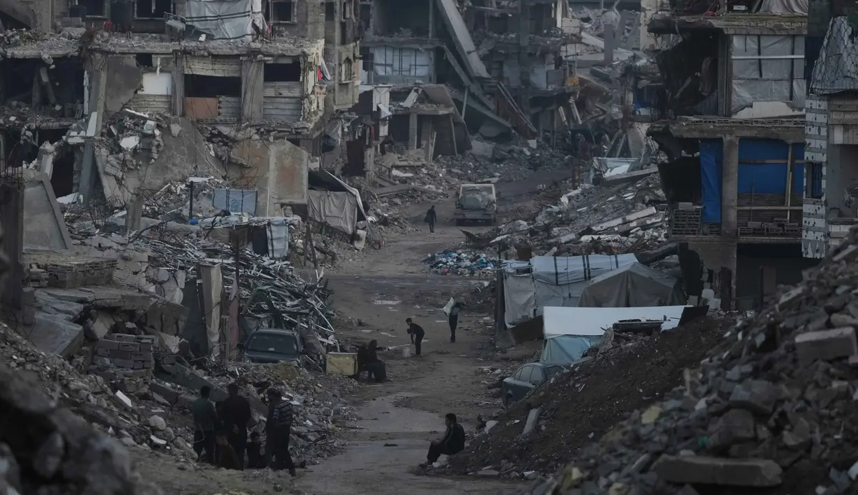 Pembukaan kembali perlintasan Rafah sangat krusial untuk mengisi kembali stok bantuan yang terkuras selama dua tahun konflik. Tampak dalam foto, warga Palestina berjalan di tengah bangunan yang hancur akibat serangan udara dan darat Israel di Kota Gaza, Selasa 6 Januari 2026. (AP Photo/Jehad Alshrafi)