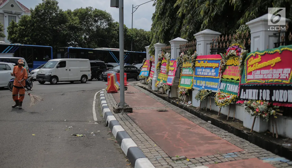 Pasukan oranye membersihkan jalan di dekat karangan bunga bertuliskan ucapan selamat untuk Joko Widodo (Jokowi) dan Ma'ruf Amin di gedung Sekretariat Negara, Jakarta, Senin (22/4). Karangan bunga tersebut ditujukan atas kemenangan Jokowi-Ma'ruf pada Pilpres 2019. (Liputan6.com/Faizal Fanani)