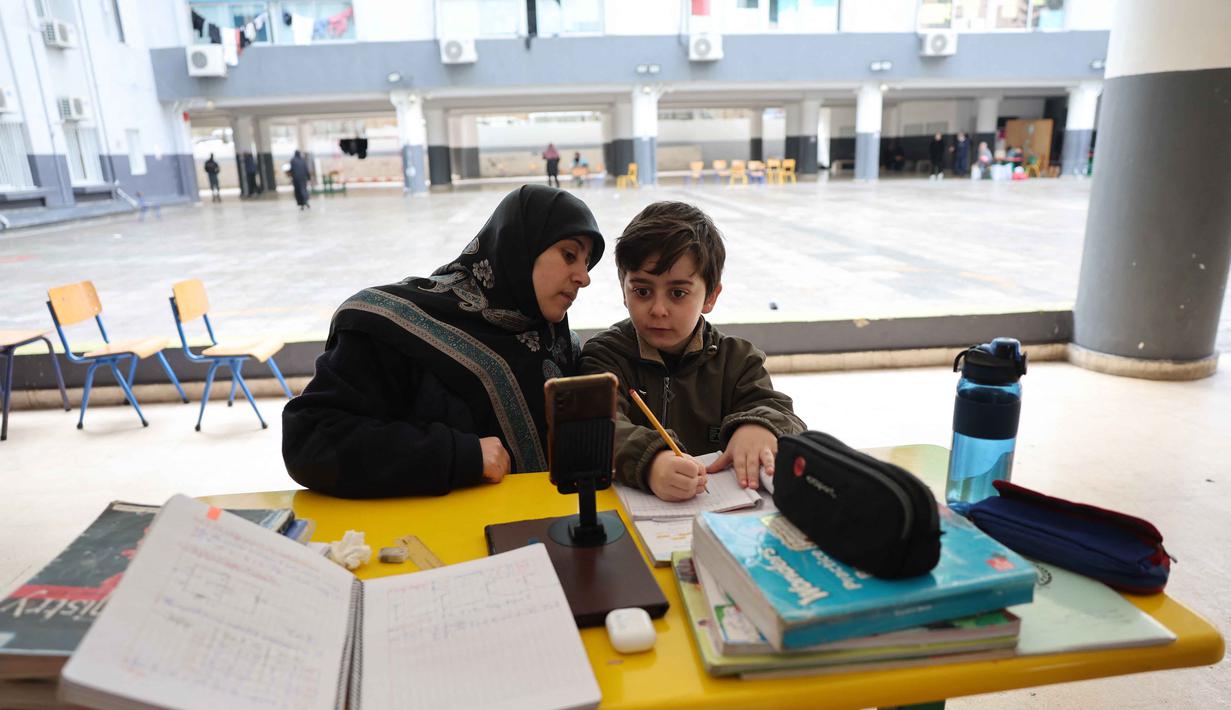 Serangan tersebut menyasar berbagai titik di wilayah perkotaan Lebanon, termasuk Beirut. Tampak dalam foto, seorang wanita Lebanon yang mengungsi duduk di samping seorang anak, mengawasi pelajaran daringnya melalui telepon seluler di sebuah sekolah negeri yang diubah menjadi tempat penampungan di kota Dekwaneh, utara Beirut, pada Rabu 25 Maret 2026. (Anwar AMRO/AFP)