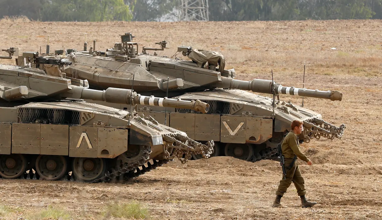 Tentara Israel berjalan melewati tank di dekat perbatasan Gaza-Israel, Jumat (19/10). Pengerahan itu disebut menjadi yang terbesar sejak perang 2014. (JACK GUEZ/AFP)