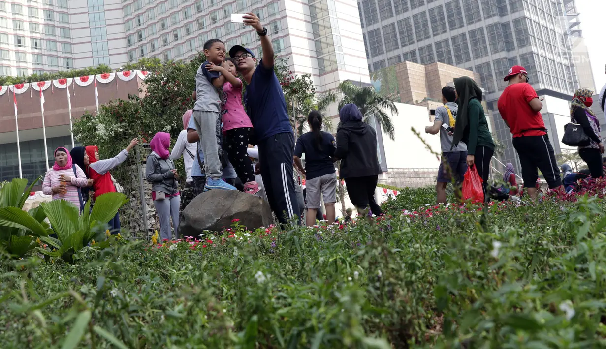 Warga berfoto bersama keluarga di area taman dekat Instalasi Gabion saat CFD di kawasan Bundaran Hotel Indonesia, Jakarta, Minggu (25/8/2019). Instalasi Gabion berdiri di lokasi bekas seni anyaman bambu Getah Getih dan diletakkan bebatuan sebagai penghias. (Liputan6.com/Helmi Fithriansyah)