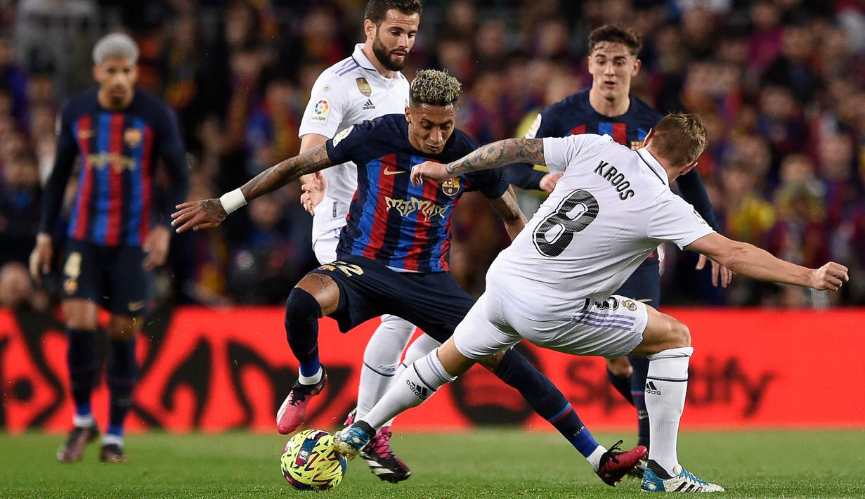 Pemain Barcelona, Raphinha (tengah) berusaha melewati pemain Real Madrid pada laga pekan ke-26 Liga Spanyol 2022/2023 di Camp Nou, Barcelona, Senin (20/03/2023). Blaugrana menang dengan skor 2-1 pada pertandingan yang bertajuk El Classico tersebut. (AFP/Josep Lago)