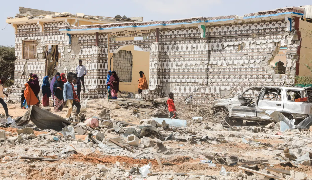 Orang-orang berjalan di sebelah rumah yang hancur dan puing-puing mobil menyusul serangan oleh militan Al-Shabaab selama penyerangan ke kantor polisi di pinggiran Mogadishu, Somalia (16/2/2022). (AFP/Hassan Ali Elmi)