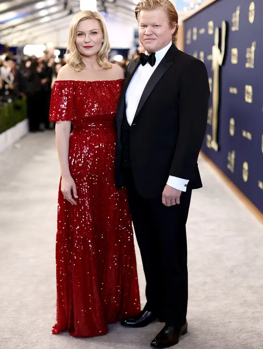 Kirsten Dunst menghadiri red carpet SAG Awards bersama pasangannya Jesse Plemons dalam balutan gaun merah off-shoulder rancangan Erdem yang berkilau. Rambut pirangnya yang lurus diikal di bagian ujung.