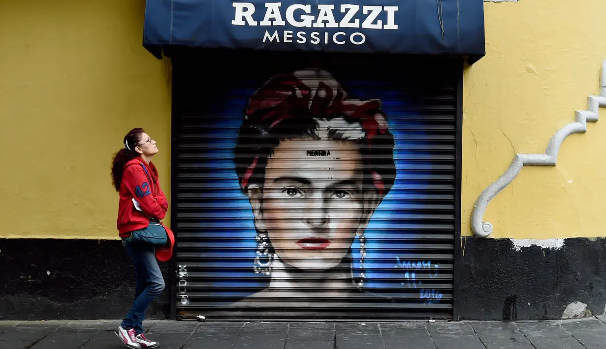 Seorang wanita melintasi mural seniman Frida Kahlo di sebuah jalan wilayah bersejarah Mexico City, Meksiko, 30 Agustus 2017. Mural menjadi salah satu langkah Pemerintah Mexico City untuk melestarikan dan mempercantik ruang publik. (ALFREDO ESTRELLA/AFP)