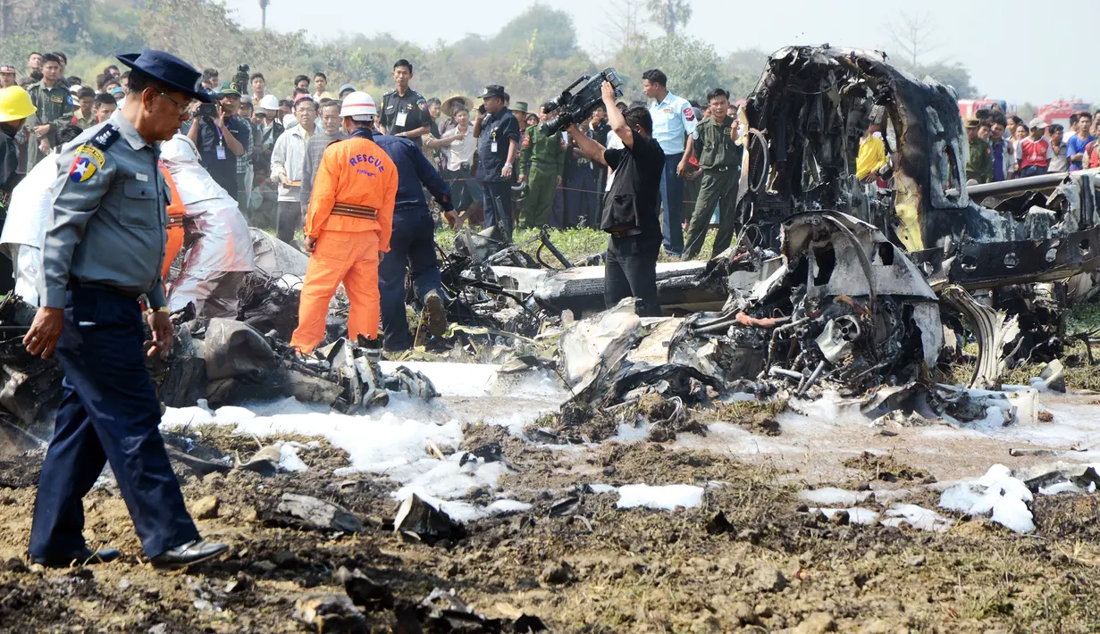 Sejumlah petugas  memeriksa lokasi jatuhnya pesawat militer sesaat setelah lepas landas dari Naypyidaw, Myanmar, Rabu (10/2). Ratusan orang berkumpul di lokasi kejadian, sementara petugas berusaha memadamkan api di badan pesawat.  (AFP/PHOTO/AUNG Htet)