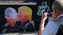 Warga mengabadikan mural bergambar calon Presiden AS, Donald Trump dan Presiden Rusia, Vladimir Putin sedang berciuman di Vilnius , Lithuania, (13/5). Mural ini dibuat sebagai sindiran terhadap Donald Trump dan Vladimir Putin. (AFP PHOTO/Petras Malukas)