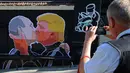 Warga mengabadikan mural bergambar calon Presiden AS, Donald Trump dan Presiden Rusia, Vladimir Putin sedang berciuman di Vilnius , Lithuania, (13/5). Mural ini dibuat sebagai sindiran terhadap Donald Trump dan Vladimir Putin. (AFP PHOTO/Petras Malukas)