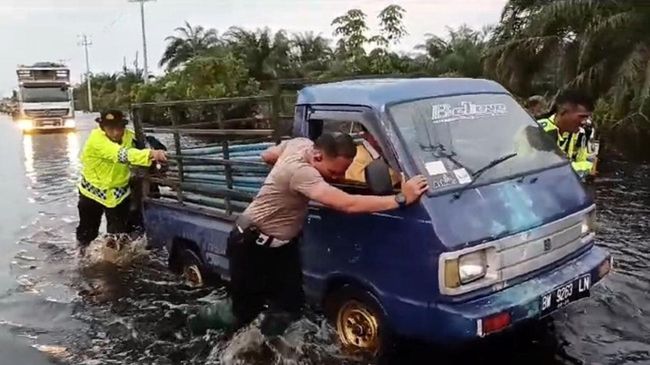 Personel Lalu Lintas Polres Pelalawan mendorong mobil mogok karena banjir di Jalan Lintas Timur Sumatra.
