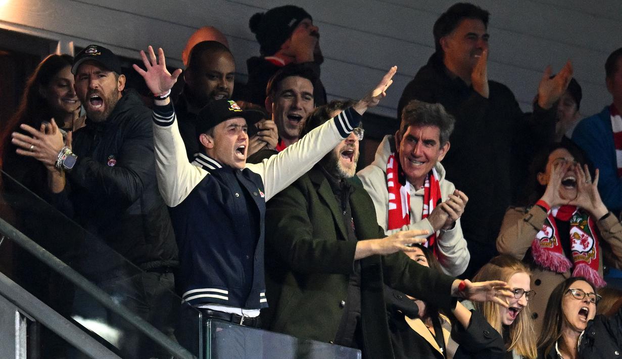 Aktor Hollywood, Ryan Reynolds (kiri) dan pemilik klub Wrexham, Rob McElhenney merayakan kemenangan timnya saat laga English National League antara Wrexham melawan Boreham Wood di Racecourse Ground Stadium, Wrexham, Wales, Sabtu (22/04/2023). Wrexham menang dengan skor 3-1 dan berhasil promosi ke Liga Dua Inggris. (AFP/Oli Scarff)