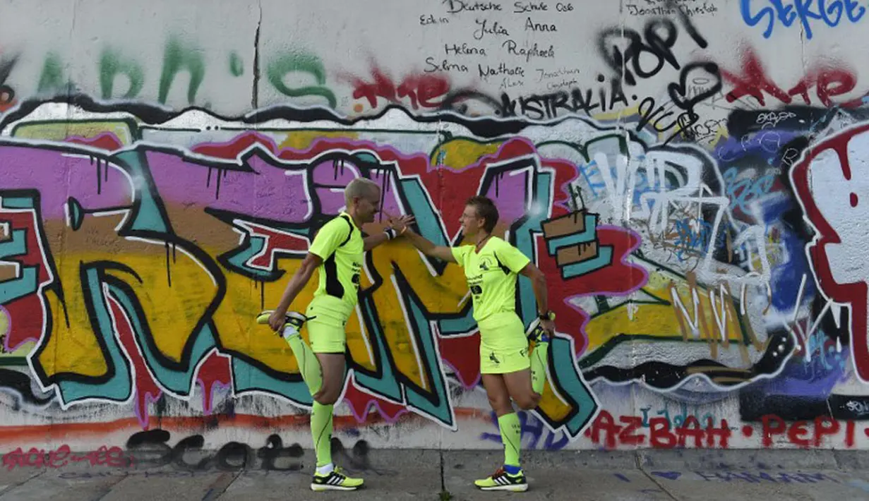 Sebuah lomba lari bertajuk "100 Meilen Berlin 2014" akan digelar di sepanjang Tembok Berlin. Tampak, Martina Schliep (kanan) dan Gaston Pruefer melakukan pemanasan sebelum latihan lari di sisi timur Tembok Berlin, (11/8/2014). (AFP PHOTO/Tobias Schwarz)