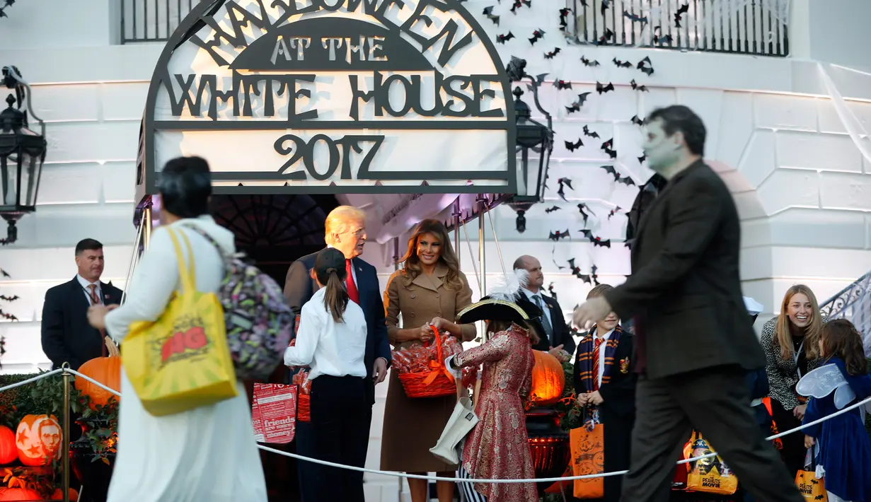 Presiden AS, Donald Trump didampingi Melania Trump membagikan permen kepada anak-anak saat open house perayaan pesta Halloween di Gedung Putih, Senin (30/10). Selain ratusan siswa, keluarga militer juga hadir di acara itu. (AP/Pablo Martinez Monsivais)