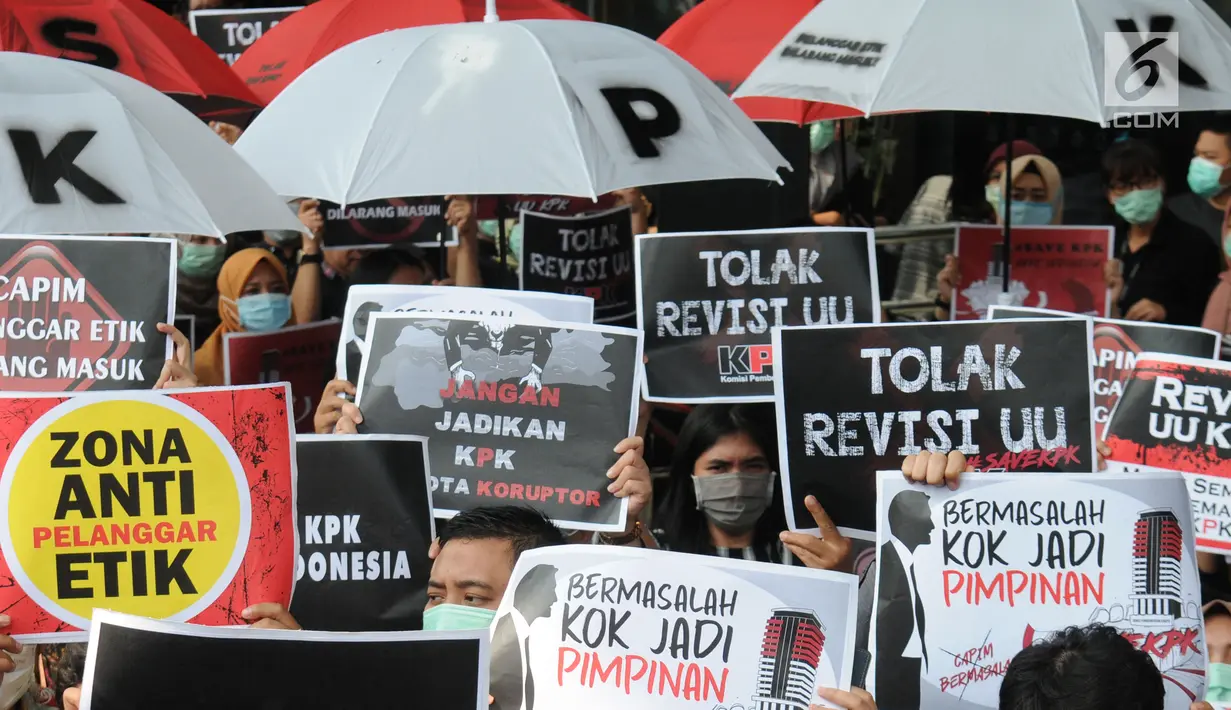 Pegawai KPK membawa poster saat menggelar aksi di Lobi Gedung KPK, Kuningan, Jakarta, Jumat (6/9/2019). Dalam aksi menolak revisi UU KPK tersebut, mereka mengenakan baju serba hitam lengkap dengan masker penutup mulut dan memasang KPK Lines di sekitar pintu masuk. (merdeka.com/Dwi Narwoko)