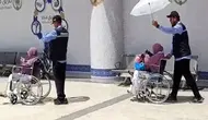 Petugas haji memayungi jemaah haji lansia yang baru tiba di Bandara Prince Mohammed bin Abdulaziz Madinah via jalur fast track. (dok. Dinny Mutiah/MCH 2025)
