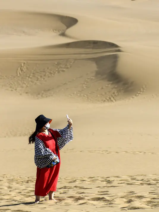 Seorang wisatawan berswafoto di kawasan wisata Gurun Kum Tag di Wilayah Shanshan, Kota Turpan, Daerah Otonom Uighur Xinjiang, China barat laut (22/9/2020). Gurun tersebut saat ini mencatat peningkatan arus wisatawan. (Xinhua/Wang Fei)