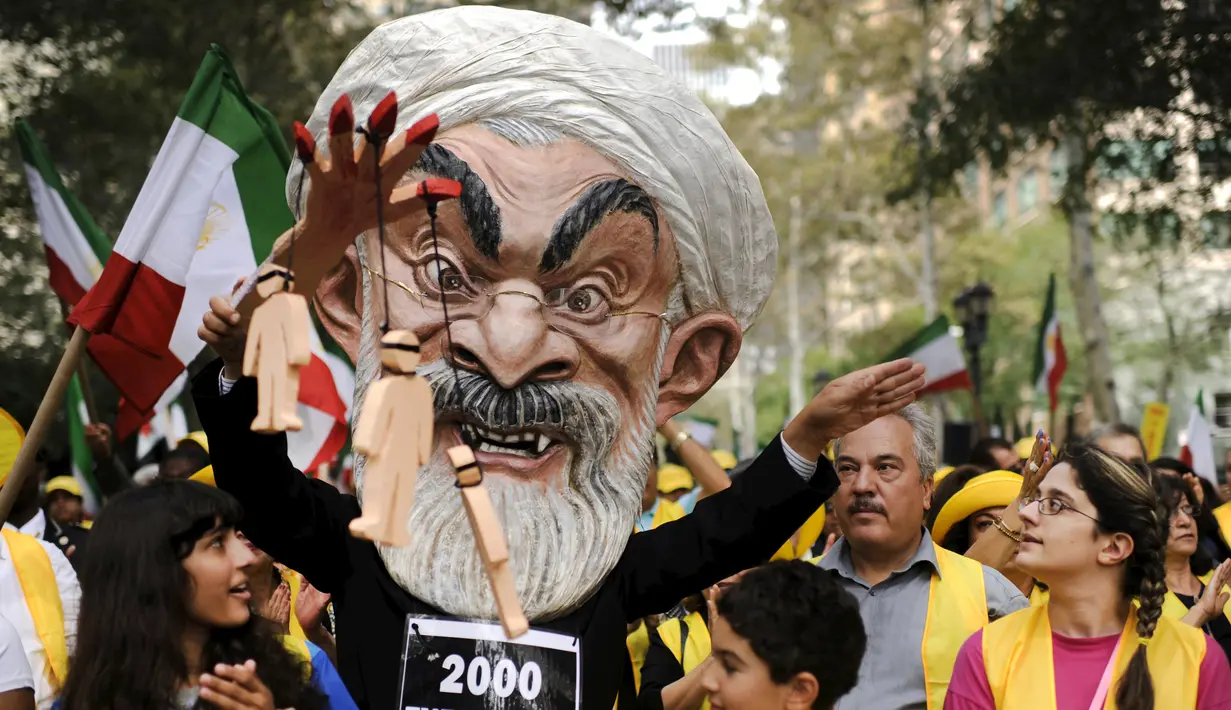 Max Saatchi berdiri dengan pengunjuk rasa lainnya sambil mengenakan topeng Presiden Iran Hassan Rouhani mengecam pelanggaran hak asasi manusia oleh pemerintah Rouhani di luar markas besar PBB, Manhattan, New York, AS (28/9/2015). (REUTERS/Darren Ornitz)
