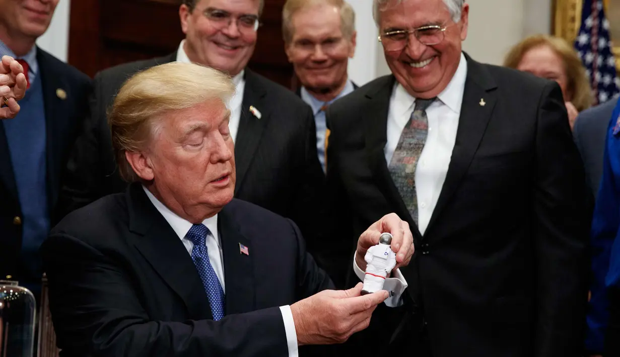 Presiden AS, Donald Trump memegang mainan Astronot setelah menandatangani sebuah kebijakan untuk mengirim astronot Amerika kembali ke bulan dan Mars di Ruang Roosevelt Gedung Putih di Washington (11/12). (AP Photo/Evan Vucci)