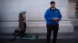 Seorang petugas keamanan berdiri di dekat Afaf Nasher yang sedang menjalankan salat di Washington Square Park di New York, AS (25/1). Afaf Nasher dikenal aktif dalam kegiatan umat muslim di New York. (AFP/Bryan R. Smith)