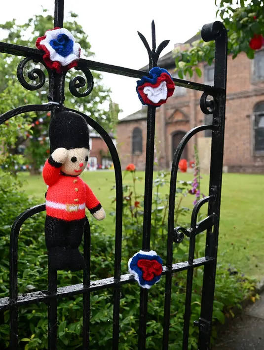 <p>Sebuah boneka penjaga Inggris rajutan terlihat terpasang di gerbang Gereja St Luke di Kapel Holmes, barat laut Inggris, pada 30 Mei 2022. Kelompok masyarakat lokal, The Holmes Chapel Community Yarn Bombers telah memenuhi desa dengan barang-barang rajutan patriotik untuk merayakan Platinum Jubilee Ratu. (Paulus ELLIS / AFP)</p>