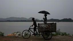 Seorang anak membonceng adiknya menggunakan sepeda gerobak saat hujan mengguyur Gauhati, India, Selasa (30/5). Beberapa negara bagian di India timur laut mengalami hujan deras sebagai efek topan Mora yang melanda selatan Bangladesh. (AP Photo/Anupam Nath)
