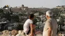 Seorang pria dan anak-anak Palestina melihat ke Masjid Kubah Batu (kiri) dan masjid Al-Aqsa (kanan), di halaman tertutup masjid Al-Aqsa, selama bulan suci Ramadan, ketika mereka menunggu panggilan untuk salat selama krisis pandemi coronavi di Kota Tua Yerusalem (19/5/2020). (AFP/Ahmad Gharabli)