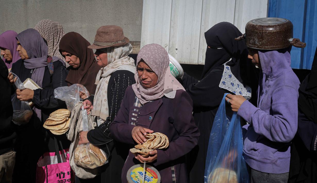 Penghalangan akses dan hambatan penyaluran bantuan ini jelas menghambat proses pemulihan situasi dan kondisi di Gaza. Tampak dalam foto, warga Palestina yang terlantar, anak-anak, dan dewasa, menunggu makanan di sebuah tempat penampungan yang telah dihuni keluarga-keluarga di Nuseirat, pusat Jalur Gaza, pada 23 November 2025. (EYAD BABA/AFP)