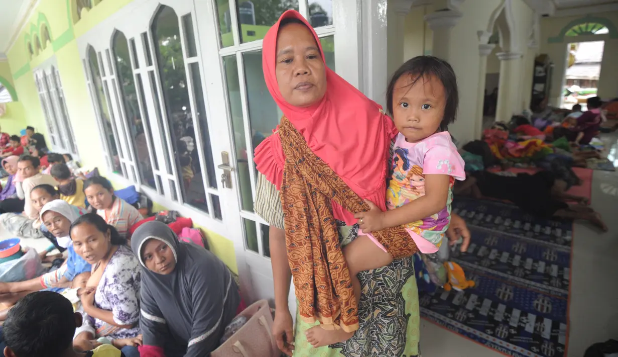 Seorang wanita menggendong anaknya saat beristirahat bersama  pengungsi bencana tsunami di sebuah masjid di Tenjolahang, provinsi Banten, Rabu (26/12). Saat ini tercatat ada 16.082 orang  mengungsi selepas tsunami Selat Sunda. (Sonny TUMBELAKA / AFP)